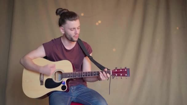 Schöner junger Mann spielt Akustikgitarre sitzend Stuhl Stoff Hintergrund — Stockvideo