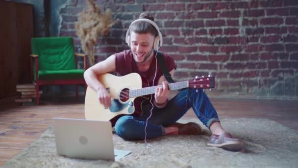 Человек акустическая гитара сидя пол с ноутбуком и наушниками играть песни онлайн уроки музыки — стоковое видео