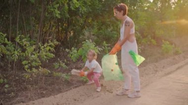 Küçük kız annesinin çevre kirliliğini önlemek için doğadaki plastik çöpleri toplamasına yardım ediyor.