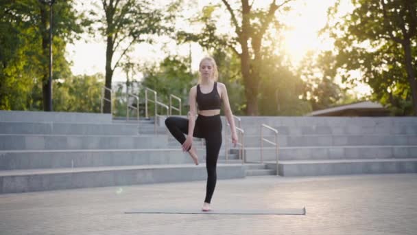 Fitness-Frau praktiziert Yoga-Übungen auf Matte im Freien City Street Sonnenlicht Hintergrund — Stockvideo