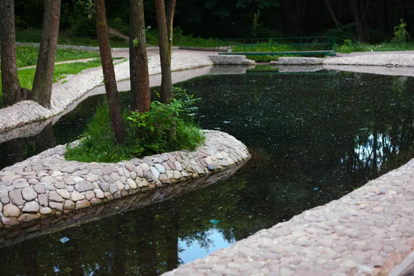 Un estanque artificial en el parque cubierto de piedras — Foto de Stock