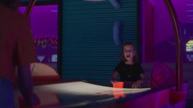 Renkli atari salonunda arkadaşlarıyla hava hokeyi oynayan heyecanlı kız arkadaşça rekabetin ve neon ışıkların keyfini çıkarıyor.
