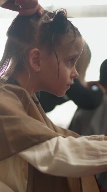 Kız kuaför koltuğunda otururken stilisti saçını dikkatlice klasik bir şilin şeklinde kesiyor. Atmosfer onun yeni görünüşü için heyecan ve heyecanla dolu..