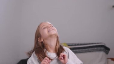 Neşeli kız dans ediyor, başını sallıyor, evde vakit geçiriyor. Sarı saçlarıyla, enerjik bir şekilde gülümsüyor ve hareket ediyor, boş zamanlarını kucaklıyor.