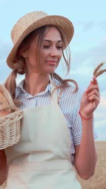 Hasır şapkalı ve önlüklü bir kadın, parlak bir gökyüzünün altında altın bir tarlada sepet taşırken gülümsüyor. Rahat tavrı, huzurlu bir kırsal kesimin güzelliğini yansıtıyor..