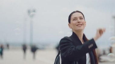 Mutlu kadın havada köpükler saçıyor, gülümsüyor ve dışarıdaki anın tadını çıkarıyor. Sahne, kabarcıklar havada süzülürken neşe ve neşe yakalıyor, çevrede eğlenceli ve canlı bir atmosfer yaratıyor.