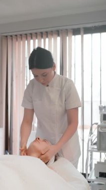 Yetenekli kozmetolojist, cilt bakımı ve genel gençleştirme tedavisi üzerine odaklanarak, parlak kaplıca ortamındaki kadın müşterilere rahatlatıcı bir masaj sağlar..