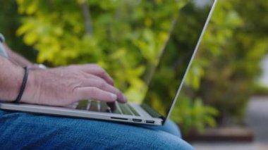 Ofis parkında oturup uzaktan çalışma, teknoloji, serbest çalışma ve modern iş dünyasını temsil eden beyaz saçlı ve sakallı kıdemli işadamının görüntüsünü büyüt.