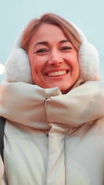 Rahat, kabarık bir palto ve kulaklık giyen bir kadın, neşeli atmosferin tadını çıkarırken ışıl ışıl gülümsüyor..