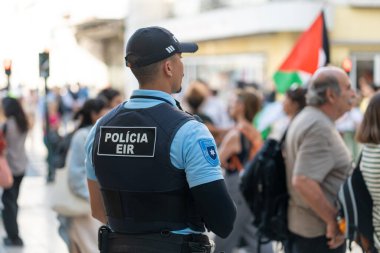 Lizbon, Portekiz 17 Haziran 2023 Üniformalı güvenlik personeli canlı bir şehir ortamında halka açık bir toplantıda nöbet tutuyor. Katılımcılar bayrakları tutuyor ve birçok insan çeşitli yönlere yürüyor,