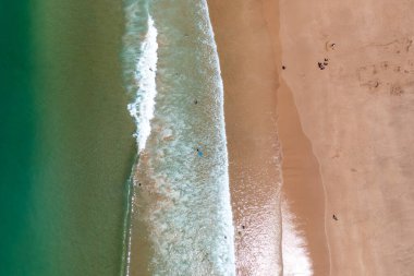 Turkuaz okyanus dalgalarının hava aracı görüntüsü geniş kumlu sahillere vuruyor güneşli yaz günlerinde huzurlu kıyı şeridini yakalıyor.