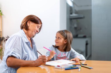 Üst düzey kadın ve torun evde birlikte kitap çizerek yaratıcı zaman geçirmenin ve ev ortamında barışçıl bir bağ kurmanın tadını çıkarıyorlar.