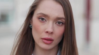 Ciddi ve ince bir ifadeyle yakından çekilmiş bir kadın portresi. Güzelce taranmış saçlarıyla doğrudan kameraya bakıyor ve sonra yana doğru bakıyor.