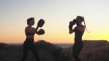 Gün batımında deniz manzaralı tepede kickboks antrenmanı yapan sportif bayan boksör. Manzaralı plaj ortamında kadın antrenörlere rehberlik ediyor.