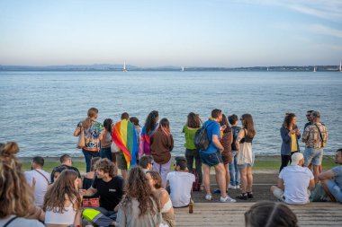 Lisbon, Portugal 17 June 2023 Participants at a vibrant LGBT parade enjoy the warm summer evening by the waterfront, proudly showcasing rainbow flags as they socialize and celebrate together.