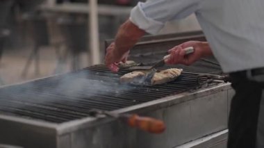 Bir şef Lizbon, Portekiz 'de mangalda taze balık pişirir. Balık pişerken duman yükselir ve lezzetli aromalar ve yerel kültürlerle dolu canlı bir atmosfer yaratır..