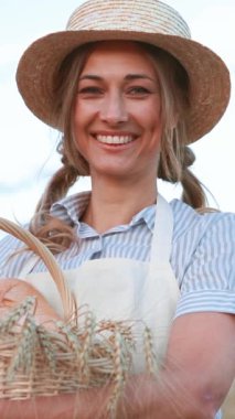 Çiftçi, güneşli bir kırsal alanda hasat edilmiş bir sepet mahsulü sergiliyor. Hasır şapka ve önlük takıyor, tarımsal yaşamın ve toplum ruhunun özünü temsil ediyor..