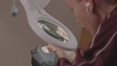 Büyüteç ve ince fırça kullanarak odaklanmış sanatçı atölyedeki bebek kafasının hassas yüz detaylarını boyuyor.