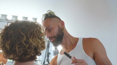 Gösteriden önce aydınlanmış giyinme odasında kadın mankene makyaj yapan odaklanmış eşcinsel profesyonel sanatçı.
