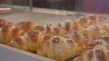 Tedarikçinin altın kruvasanları kafedeki fırın vitrininde düzenleyen maşalarla yakın plan fotoğrafı. Hepsi çok lezzetli ve lezzetli görünüyor.