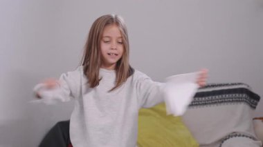 Neşeli kız kağıtları yırtıyor ve onları evdeki havaya fırlatıyor, neşeli bir ortamda eğlenirken heyecanla gülümsüyor.