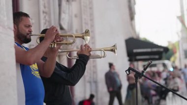 Portekiz, Lizbon 25 Haziran 2025 Yoldan geçenleri Lizbon 'da enerjik trompet müziğiyle eğlendiren iki müzisyen. Renkli binalar ve heyecanlı kalabalık öğleden sonra boyunca davetkar bir sokak atmosferi yaratıyor..