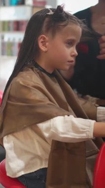 Liseli bir kız kuaför koltuğunda otururken bir stilist klasik bir bob yaratmak için saçını dikkatlice kesiyor. Samimi çocuklar kuaför deneyimi eğlenceli ve eğlenceli kılıyor..