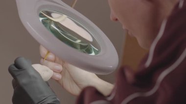 Eldivenli ressam büyüteç altında silikon bebek yüzü çiziyor, hassas çalışmalara odaklanıyor ve el yapımı minyatür figürlerle güzel özellikler yakalıyor.