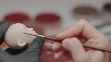 El yapımı oyuncak bebek kafası üzerine hassas yüz hatları çizmek için fırça kullanan yetenekli sanatçıların yakın çekimi.