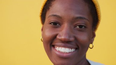 Sarı arka planda sarı şapkalı gülümseyen siyah kadın portresi. Kameraya bakan kendine güveni tam genç bir bayan.