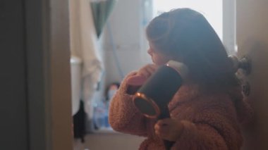 Sabah rutini sırasında evde saç fırçalayan ve kurutan küçük bir kız. Çocukluğu ve kendine bakımı gösteren rahat bir ev hayatı.