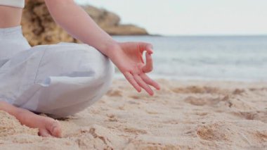 Kadının, deniz kenarındaki kumlu kumsalda elinde meditasyon hareketiyle nilüfer tozu pratiği yaptığı yakın plan. Huzuru, sakinliği ve farkındalığı kucaklamak