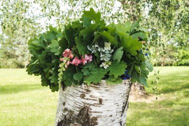 summer solstice wreath of oak branches and flowers on a birch block clipart