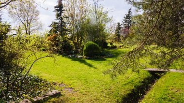 Baharda kırsalda, hendeğin sağ tarafında bir yaya köprüsü olan süs bahçesi.