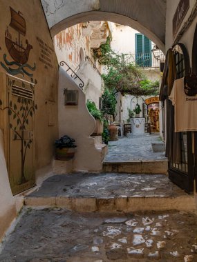 Sperlonga, İtalya - 05.02.2025: Merdivenli bir yürüyüş yolu ve evler arasında avluya uzanan bir kemer. Duvarda dekoratif çizimler var. Bir sürü saksı ve bitki..