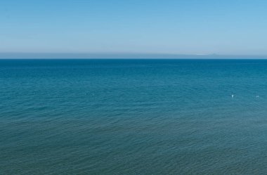 Mavi bir deniz yüzeyinin havadan görünüşü, beyaz martıların yüzüşü, su dokusu, ön planda sığ su, ufukta görünen dağlar mavi bir gökyüzü arka planına karşı..