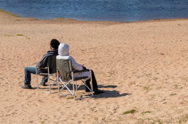 Çift güneşli bir öğleden sonra plajda katlanan sandalyelerde oturur..