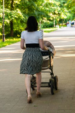 Genç bir kadın bir yaz günü bebek arabasıyla yürür. Arkadan görünüm