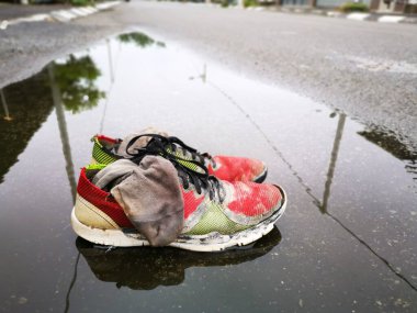 Yol kenarındaki su birikintisinde yıpranmış spor ayakkabı ve çorap..