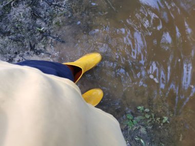 Bilinmeyen kişi sarı çizme giyiyor, sel basmış çiftliğe doğru yürüyor..