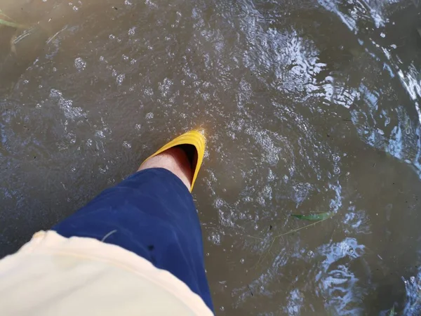 穿着黄色靴子走进被水淹没的农场的身份不明的人 — 图库照片