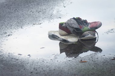 Yol kenarındaki su birikintisinde yıpranmış spor ayakkabı ve çorap..