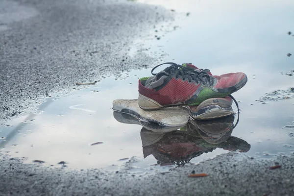 worn out sneaker and stocking on the roadside\'s puddle.