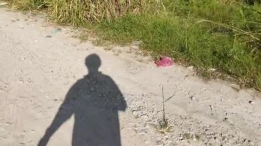 Tanımlanamayan kişinin gölgesi kırsal yolda gündüz yürüyor.
