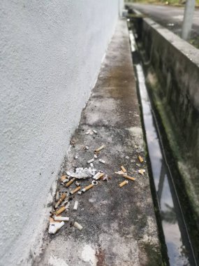 Kirli su giderinin köşesinde sigara izmaritleri var..