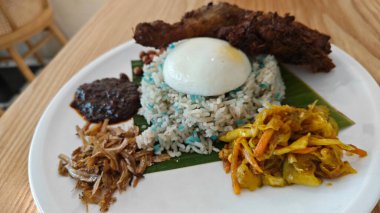 a plate of Blue Butterfly Pea nasi lemak rice with fried chicken drumstick,pickle vegetable,anchovies,peanuts and sambal. 