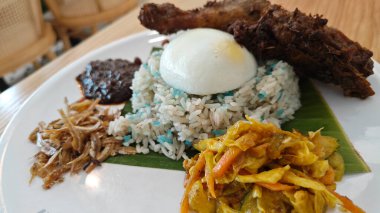 a plate of Blue Butterfly Pea nasi lemak rice with fried chicken drumstick,pickle vegetable,anchovies,peanuts and sambal. 