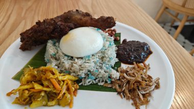 a plate of Blue Butterfly Pea nasi lemak rice with fried chicken drumstick,pickle vegetable,anchovies,peanuts and sambal. 
