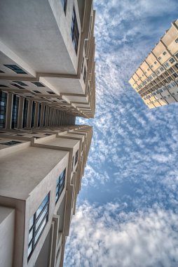 looking up high the cloudy blue sky with the high rise building in the foreground.  