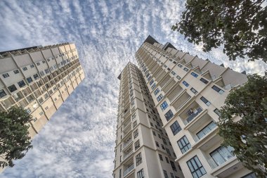 looking up high the cloudy blue sky with the high rise building in the foreground.  